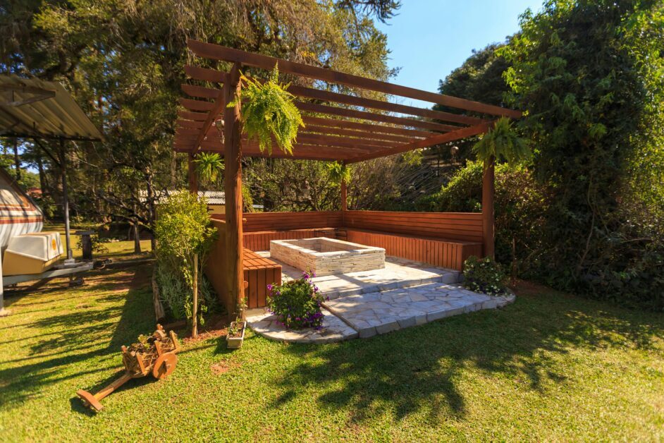 Spacious wooden gazebo in a lush garden setting with green foliage and stone flooring.