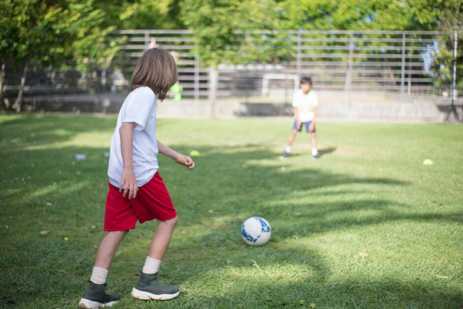 Two children playing soccer outside, enjoying a sunny day.