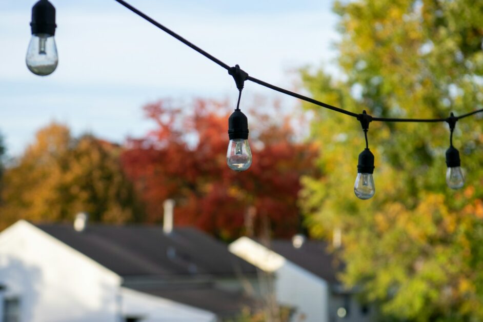 String lights hang above houses with fall foliage.